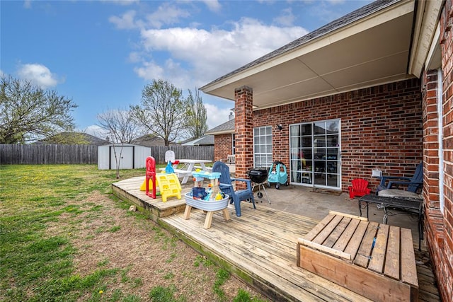 wooden terrace featuring a fenced backyard, a storage unit, an outbuilding, a yard, and outdoor dining space