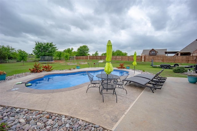 view of pool featuring a lawn, fence, a trampoline, and a patio area
