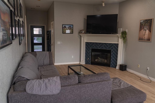living area featuring a tiled fireplace, baseboards, and wood finished floors