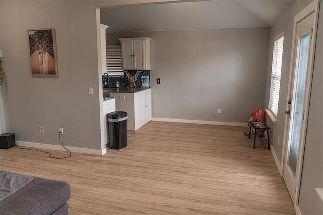kitchen featuring decorative backsplash, baseboards, lofted ceiling, light wood-style floors, and white cabinetry