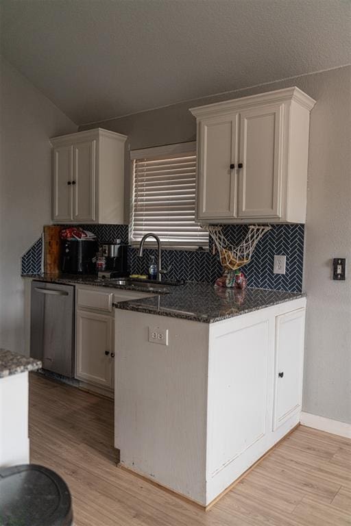 kitchen featuring backsplash, stainless steel dishwasher, light wood-type flooring, a sink, and dark stone countertops