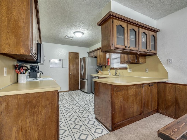 kitchen with a textured ceiling, a sink, light countertops, a peninsula, and glass insert cabinets
