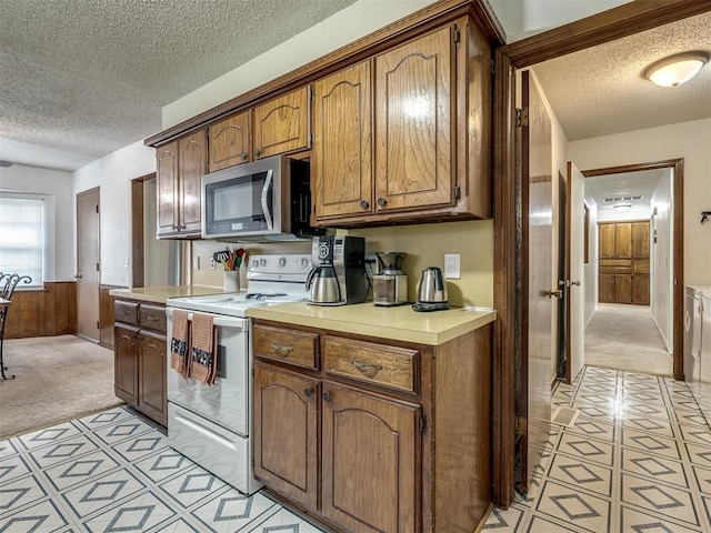 kitchen with white range with electric cooktop, stainless steel microwave, a textured ceiling, and light carpet