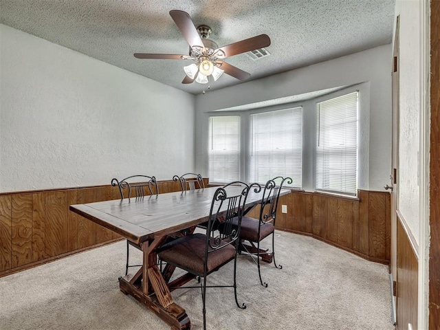 dining space featuring wooden walls, light carpet, a ceiling fan, and a textured ceiling