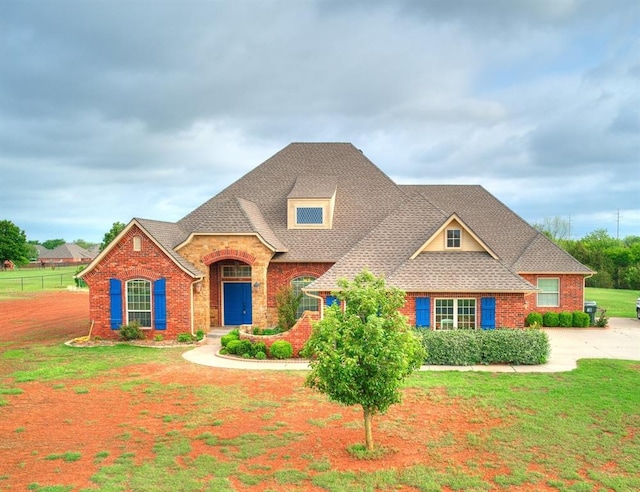 view of front of house with brick siding, fence, roof with shingles, and a front lawn