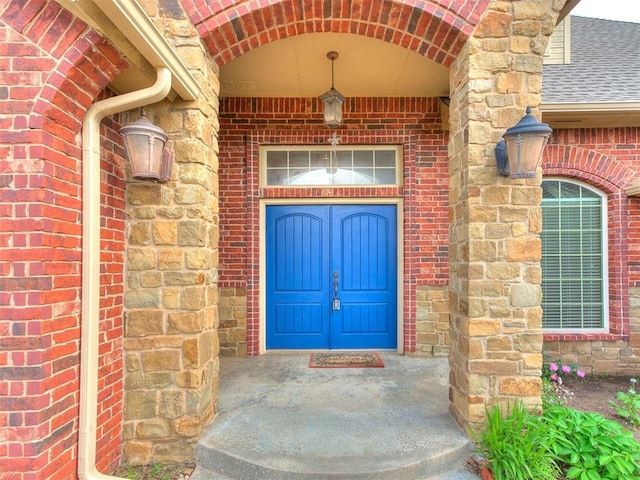 property entrance featuring a shingled roof, stone siding, and brick siding