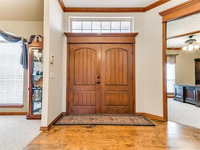 carpeted foyer featuring baseboards, ornamental molding, wood finished floors, and a wealth of natural light
