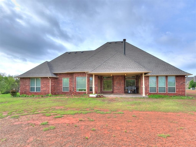 back of house featuring brick siding, a patio, a shingled roof, and a lawn