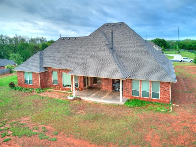 back of property featuring roof with shingles, a yard, a patio area, and brick siding