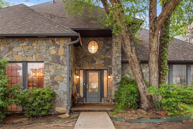 entrance to property with a shingled roof and stone siding