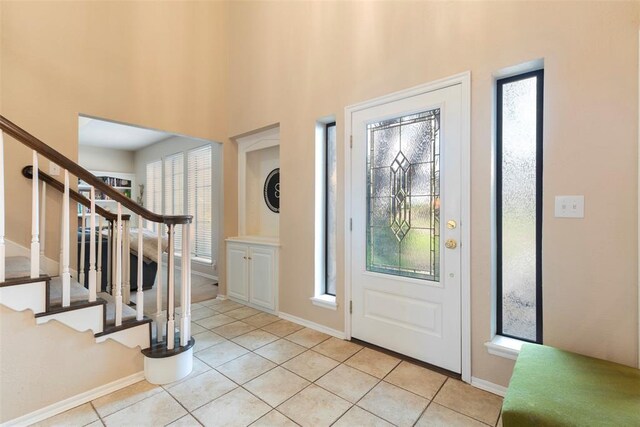entrance foyer with stairs, baseboards, light tile patterned floors, and a towering ceiling