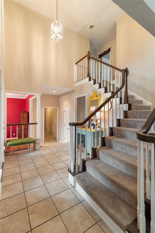 stairs with tile patterned floors, a high ceiling, baseboards, and visible vents