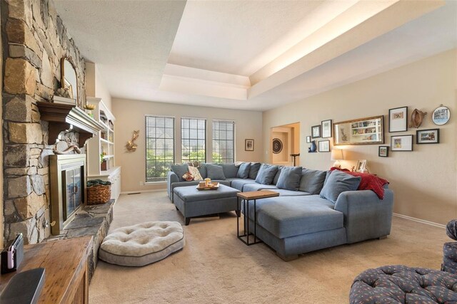 carpeted living room with baseboards, a tray ceiling, and a fireplace