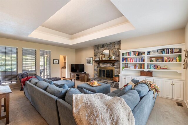 living room featuring a stone fireplace, visible vents, light carpet, and a raised ceiling