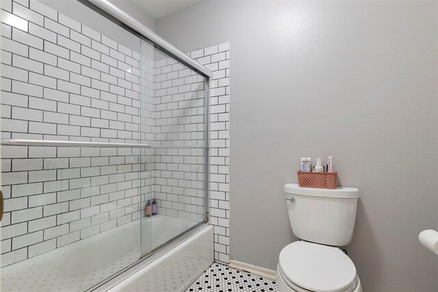 bathroom featuring bath / shower combo with glass door, baseboards, and toilet