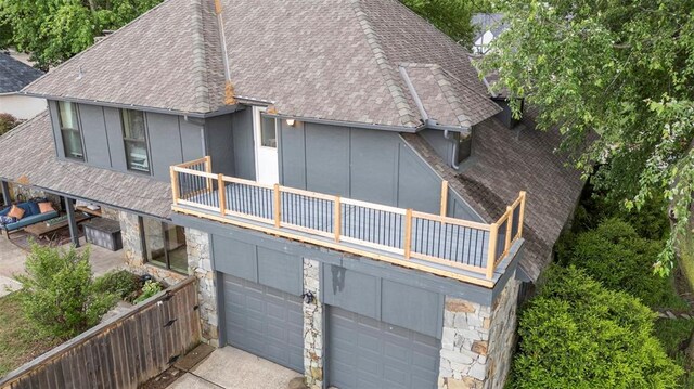 back of house featuring a garage, stone siding, roof with shingles, and a balcony
