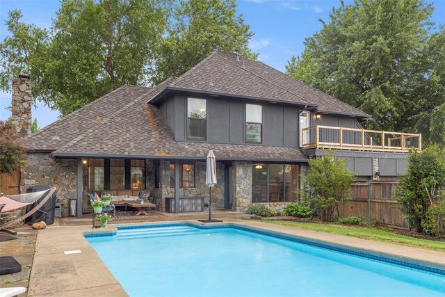 rear view of property with fence, a shingled roof, stone siding, outdoor lounge area, and a fenced in pool