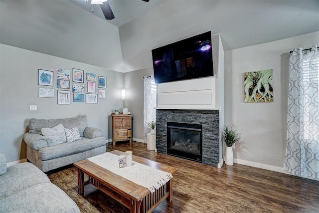 living area featuring baseboards, a ceiling fan, wood finished floors, and a stone fireplace
