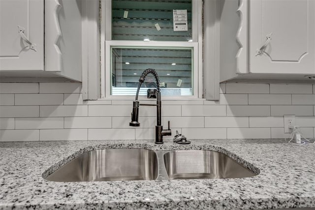 interior details with a sink, white cabinetry, backsplash, and light stone countertops