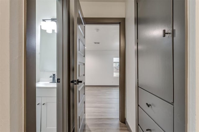 hallway with a sink, light wood-style floors, and visible vents