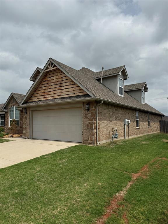 view of front facade featuring a front yard, brick siding, a shingled roof, an attached garage, and driveway