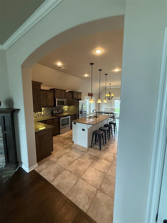 kitchen with dark brown cabinets, a sink, arched walkways, stainless steel appliances, and ornamental molding