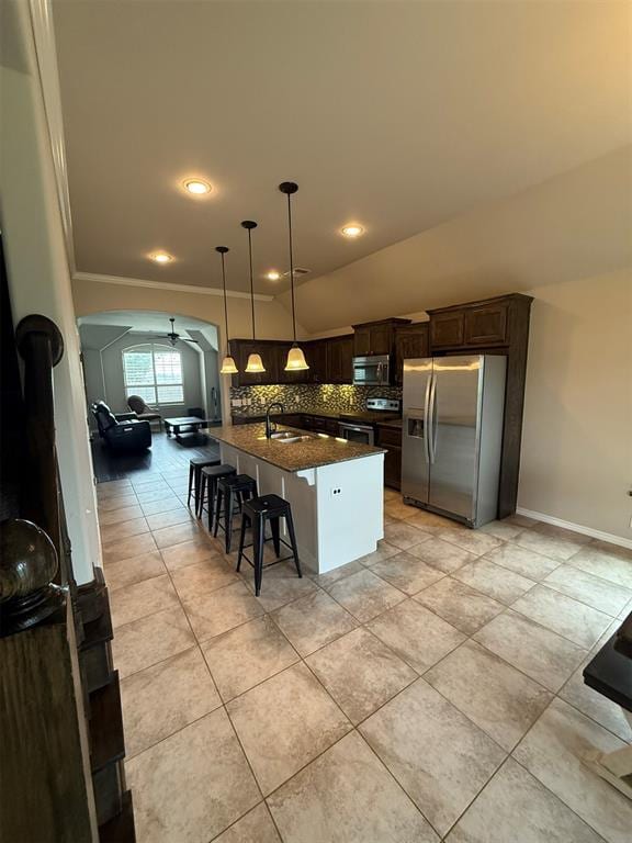kitchen featuring a breakfast bar area, a ceiling fan, appliances with stainless steel finishes, tasteful backsplash, and arched walkways