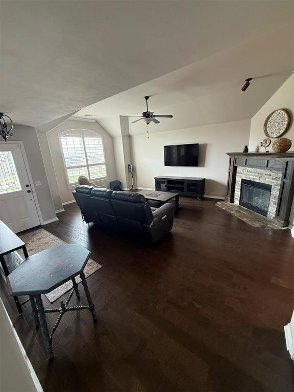 living room featuring ceiling fan, a stone fireplace, wood finished floors, baseboards, and lofted ceiling