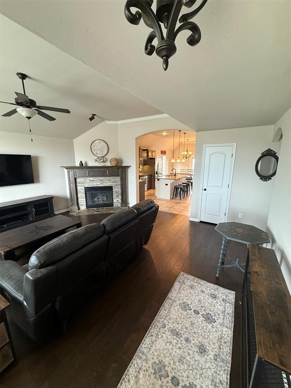 living room featuring dark wood-style flooring, arched walkways, a fireplace, vaulted ceiling, and ceiling fan with notable chandelier