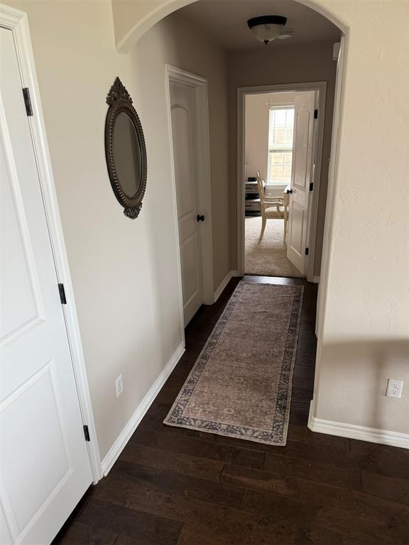 hall with arched walkways, baseboards, and dark wood-style floors
