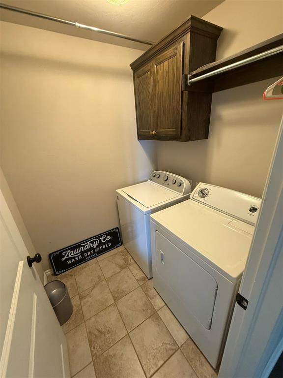 laundry room with cabinet space, light tile patterned floors, and washing machine and clothes dryer