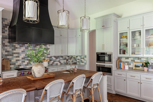 kitchen featuring a sink, premium range hood, decorative backsplash, and pendant lighting