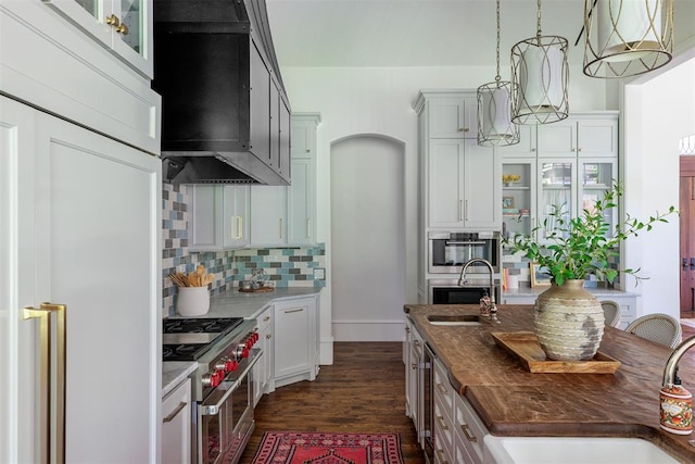kitchen with range with two ovens, wall chimney exhaust hood, decorative backsplash, a sink, and dark wood-style floors