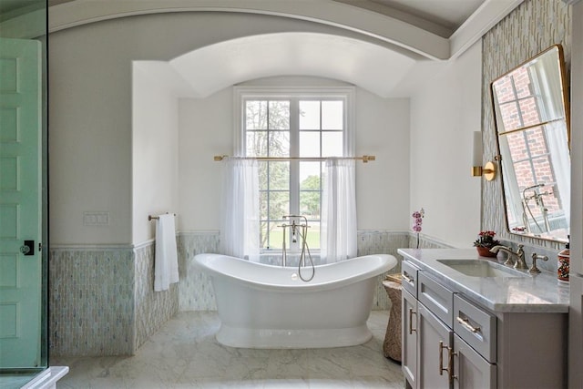 full bathroom featuring a wainscoted wall, vanity, a freestanding tub, tile walls, and marble finish flooring