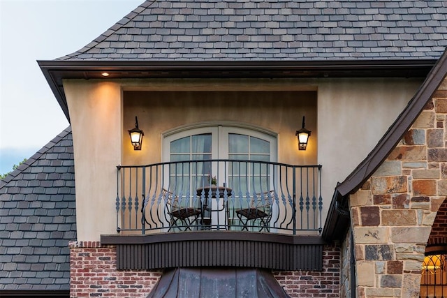 view of exterior entry with stucco siding, a balcony, and brick siding