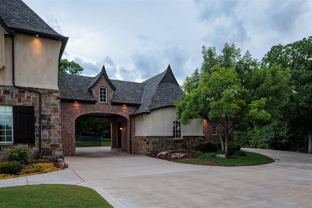 view of front of house featuring stone siding, driveway, and a high end roof