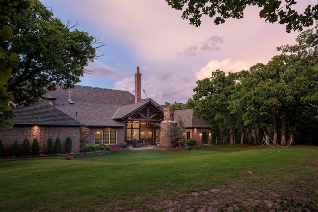 back of house at dusk with a lawn, a patio area, a chimney, and brick siding