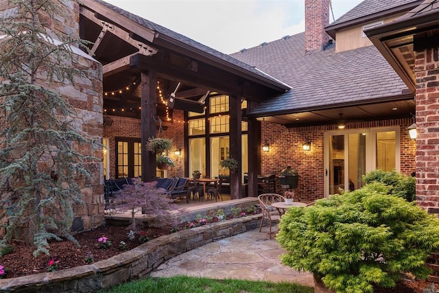 property entrance with a patio, a high end roof, brick siding, and a chimney