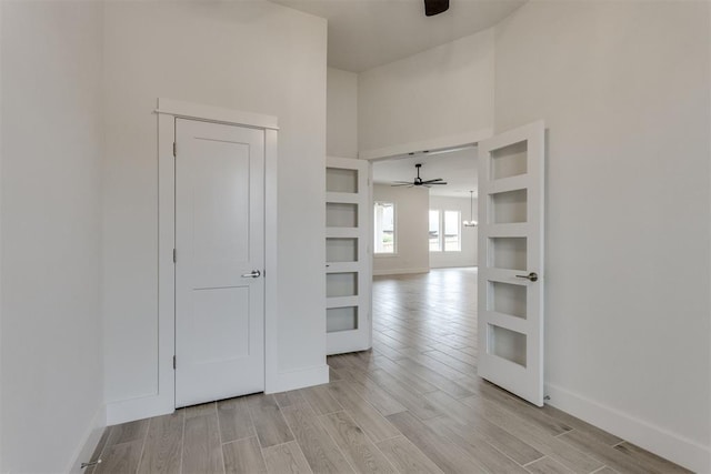 unfurnished room featuring baseboards, a ceiling fan, light wood-style flooring, and a towering ceiling