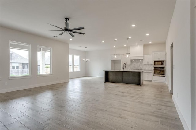 unfurnished living room featuring recessed lighting, a sink, baseboards, and ceiling fan with notable chandelier