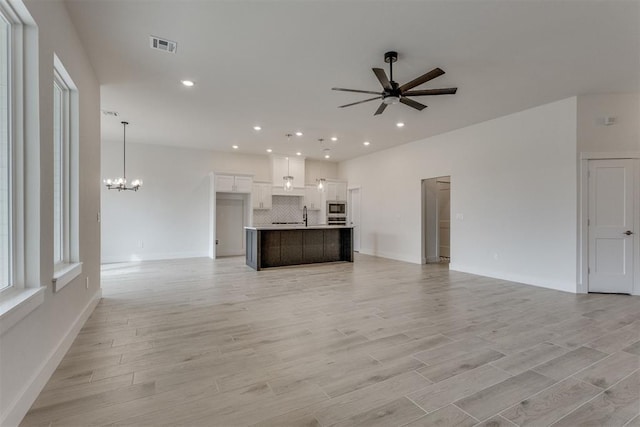 unfurnished living room with ceiling fan with notable chandelier, recessed lighting, baseboards, light wood-type flooring, and visible vents