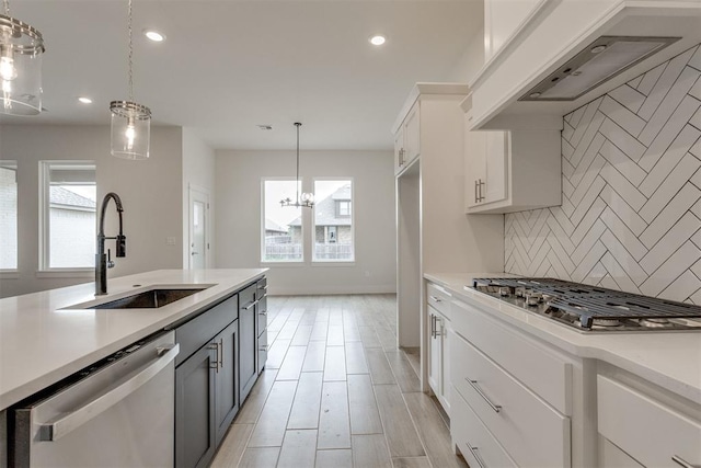 kitchen with light countertops, wall chimney exhaust hood, tasteful backsplash, a sink, and appliances with stainless steel finishes