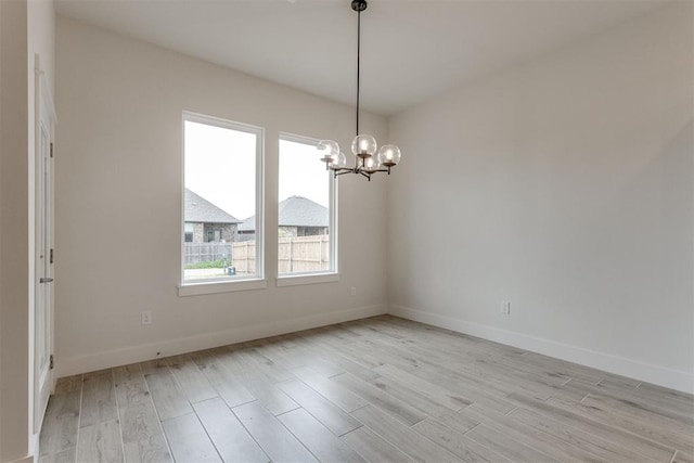 unfurnished room featuring baseboards, an inviting chandelier, and light wood-style flooring