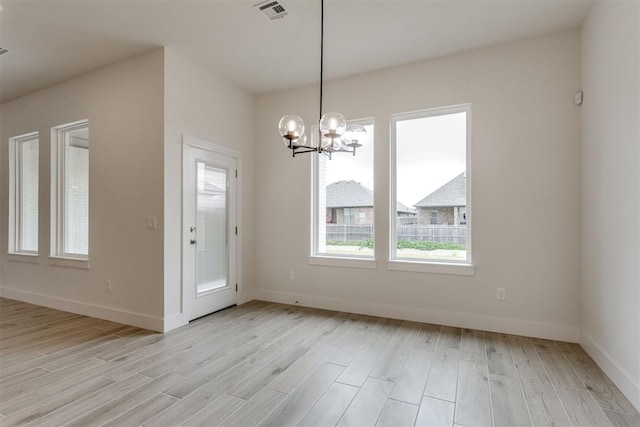 unfurnished dining area with visible vents, light wood-style flooring, baseboards, and a notable chandelier