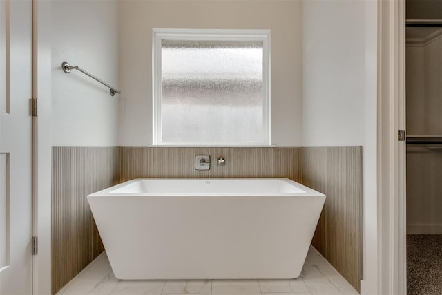 bathroom with a soaking tub, marble finish floor, and a wainscoted wall