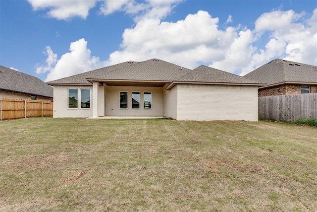 rear view of property featuring a fenced backyard, a lawn, roof with shingles, and brick siding