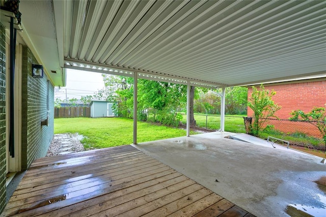 wooden deck with a storage unit, a fenced backyard, an outbuilding, a patio area, and a lawn
