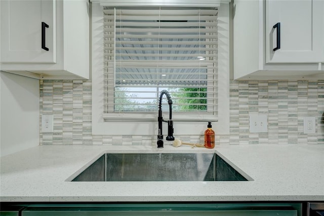 kitchen featuring light stone counters, a sink, white cabinetry, and backsplash