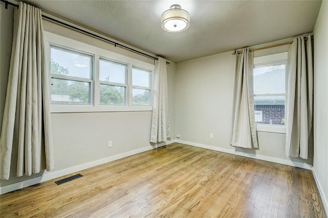 unfurnished room featuring baseboards, a textured ceiling, wood finished floors, and visible vents