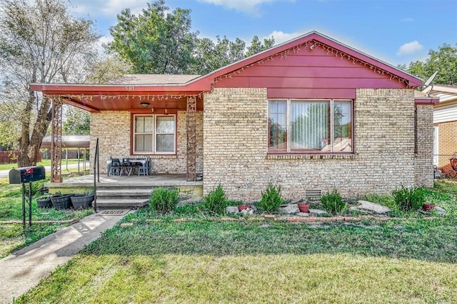 bungalow with a porch, brick siding, and a front lawn